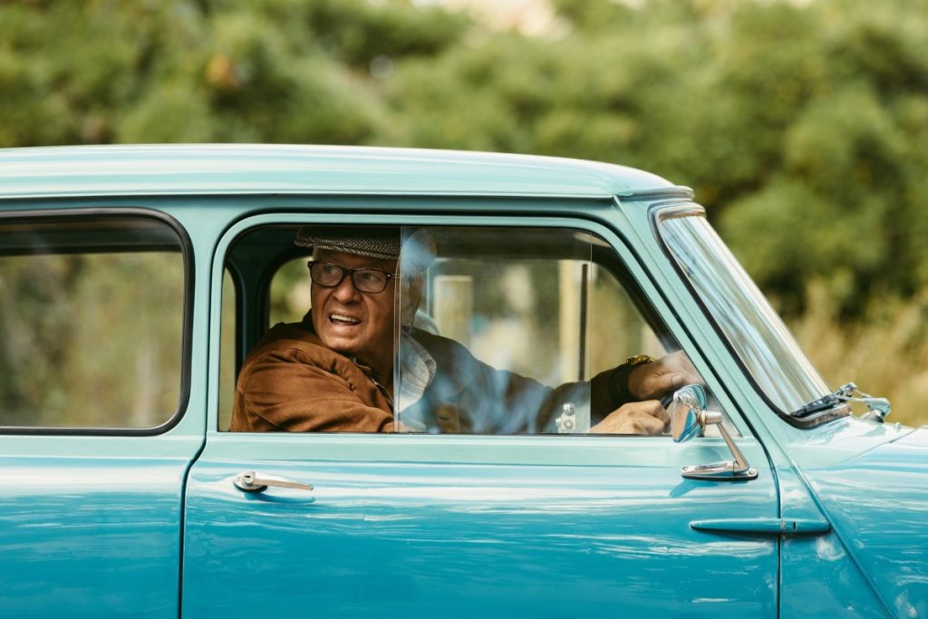 An elderly man drives a vintage car.