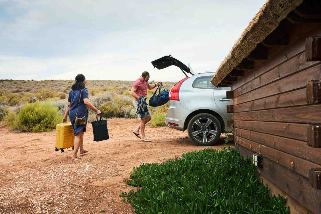 Couple packing their luggage into the trunk of their car after a summer vacation together at a cabin in a nature reserve.