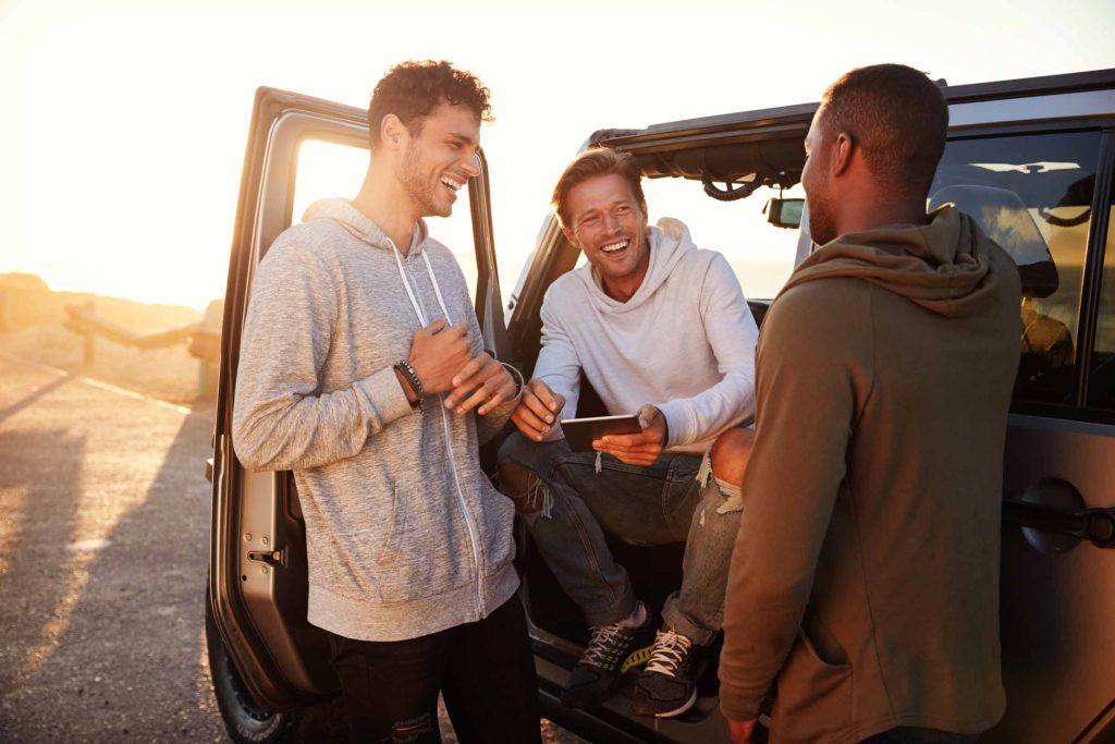 Three male friends on a road trip using a tablet computer.