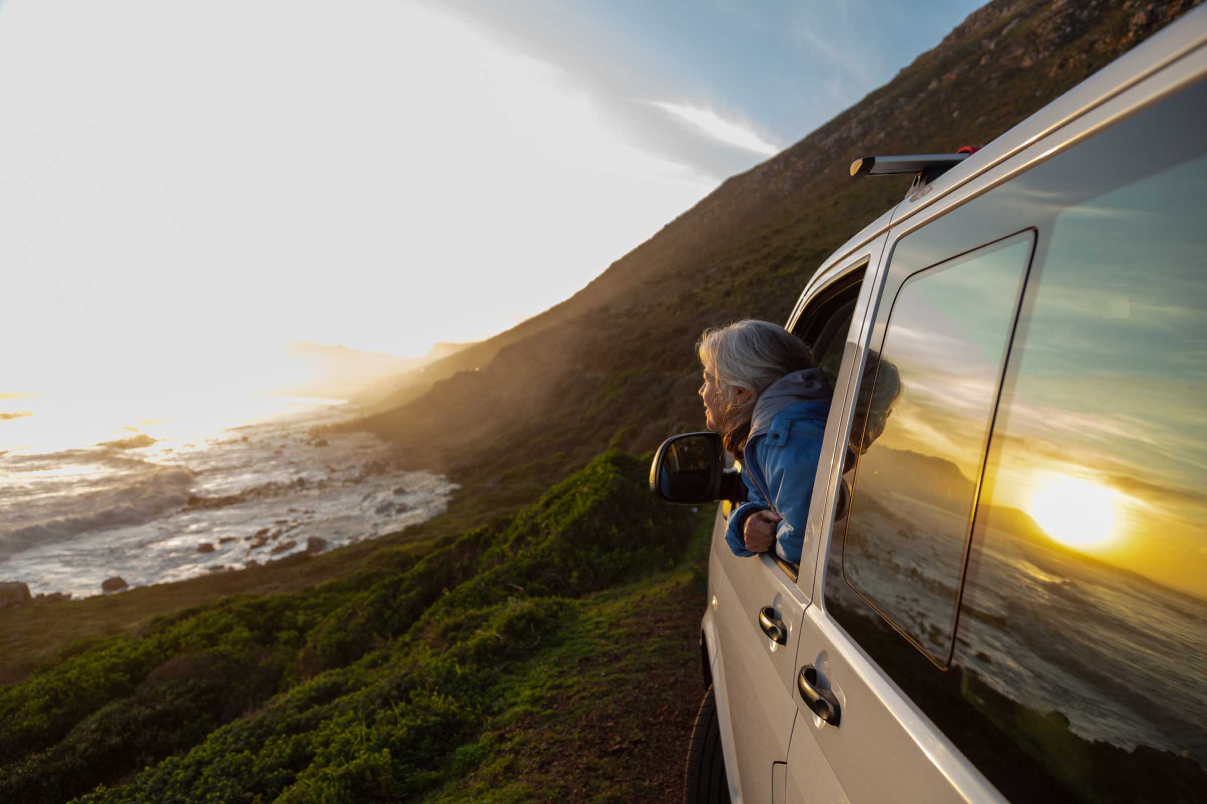 Senior woman watching sunset from her camper van